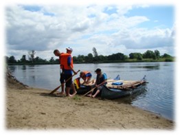 junge Menschen mit Paddeln und Schwimmwesten warten am Ufer eines Sees darauf, dass sie mit dem selbstgebauten Floß losfahren können. 